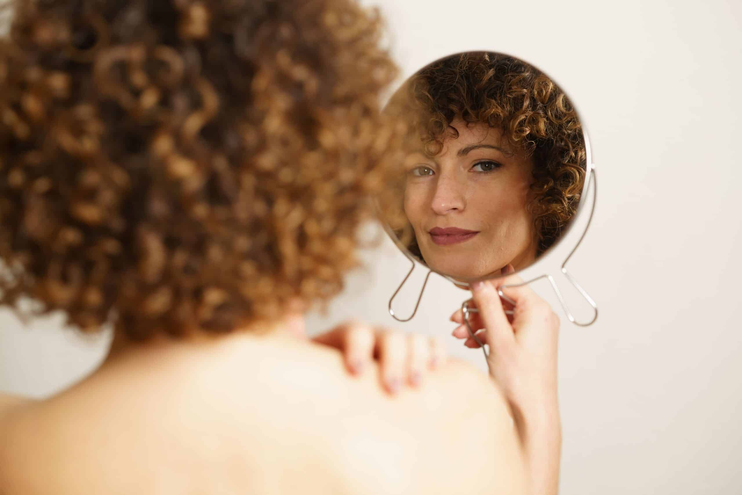 Woman looking in a mirror at sagging skin along her cheek and jawline during a skin consultation